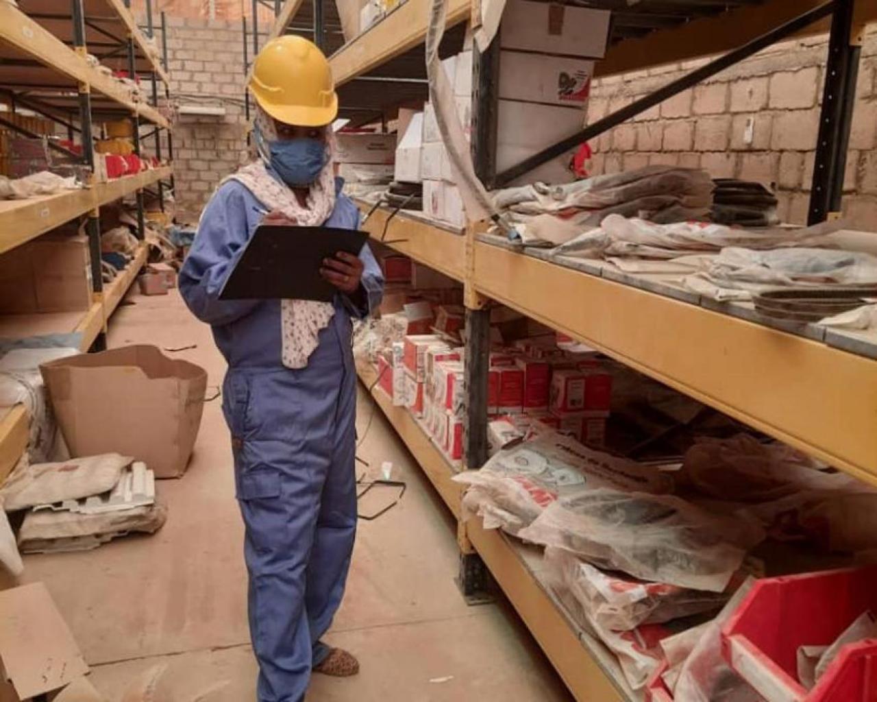 A woman in work attire looks down at a clipboard in a warehouse.