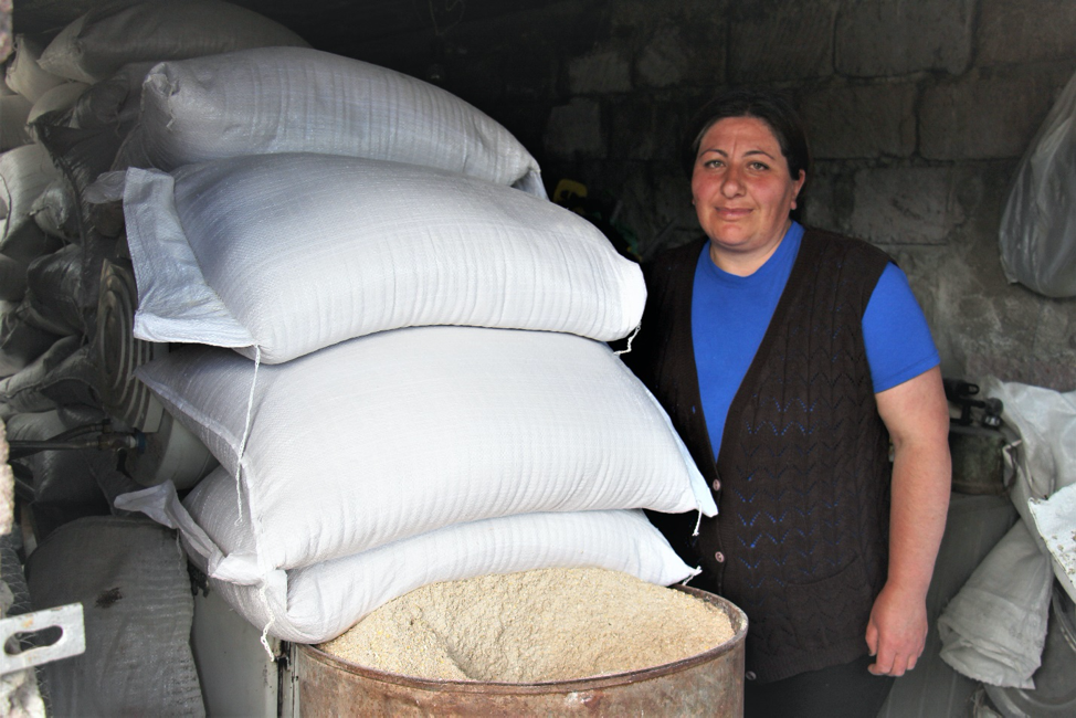 Una mujer se encuentra junto a una gran pila de sacos blancos.