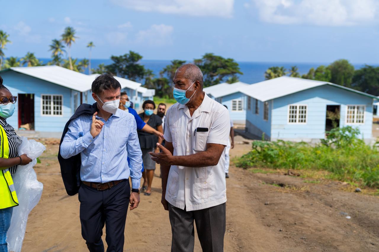 Didier Trebucq, le Coordonnateur résident des Nations Unies pour la Barbade et les Caraïbes orientales, discute avec un homme en marchant sur un sentier bordé de maisons en bois bleues en cours de construction, à Saint-Vincent-et-les-Grenadines