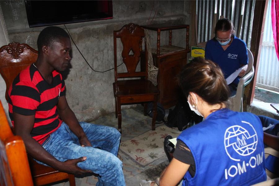 Un homme haïtien est interviewé par deux members du personnel de l'OIM dans une pièce sombre.