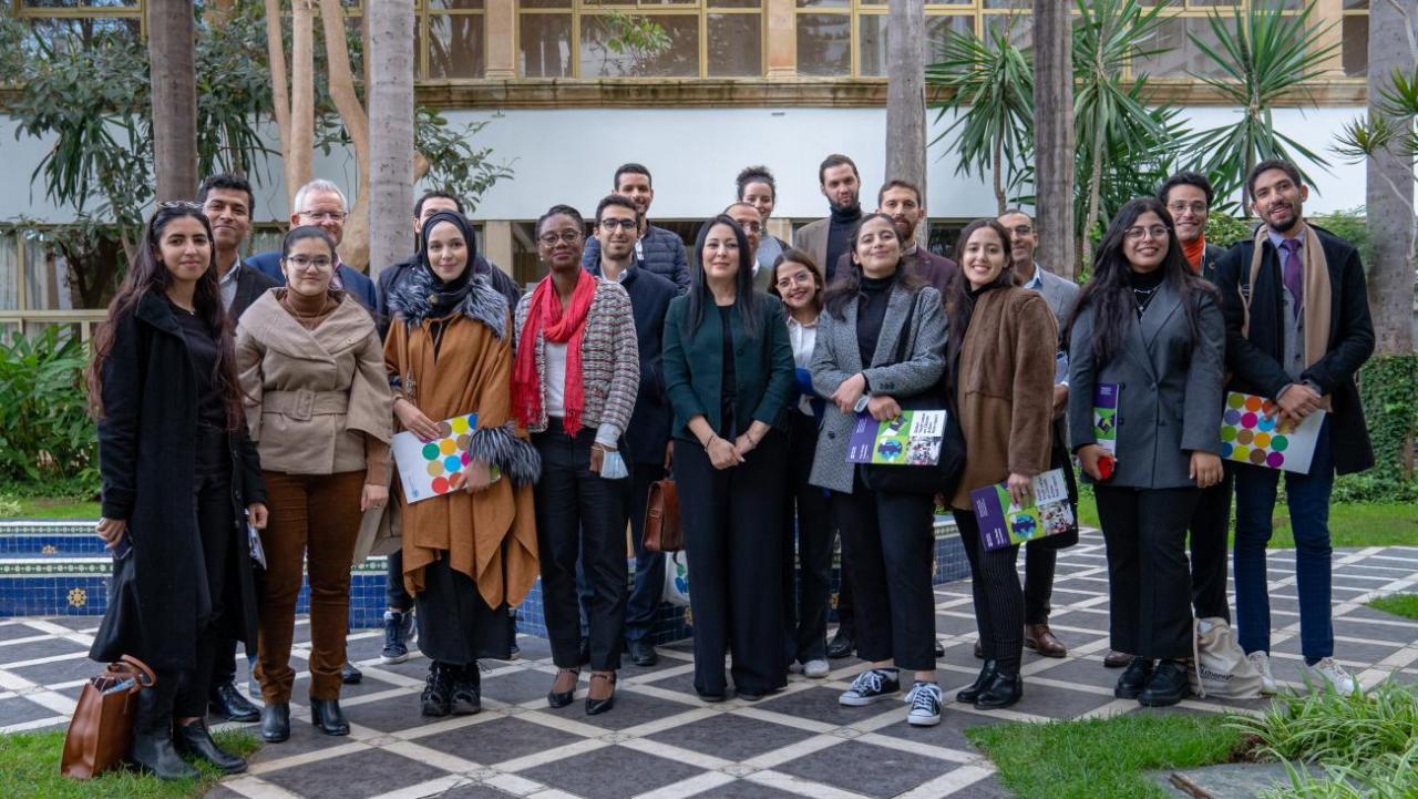 A group of people stand in a group outside and smile at the camera. 