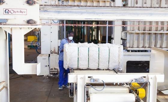 A person in a face mask works on a large cotton bail in a factory. 