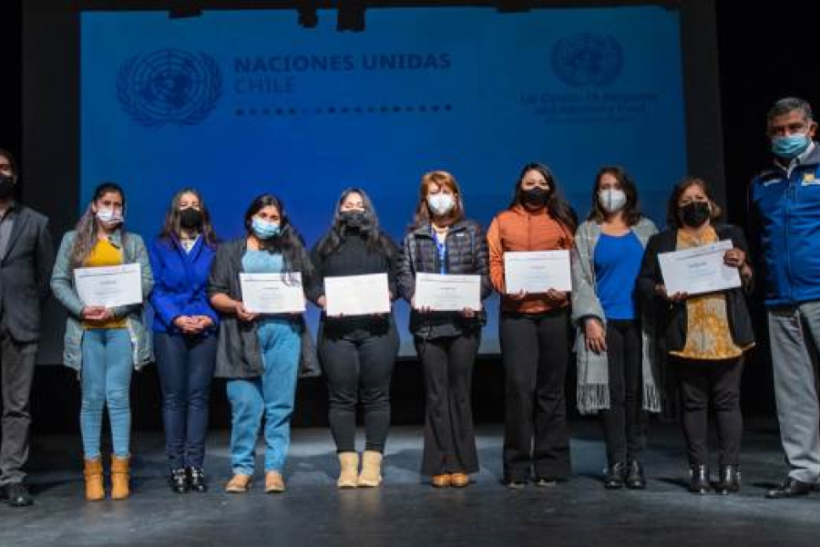 A group of women are standing next to each other on a stage and holding their diplomas.