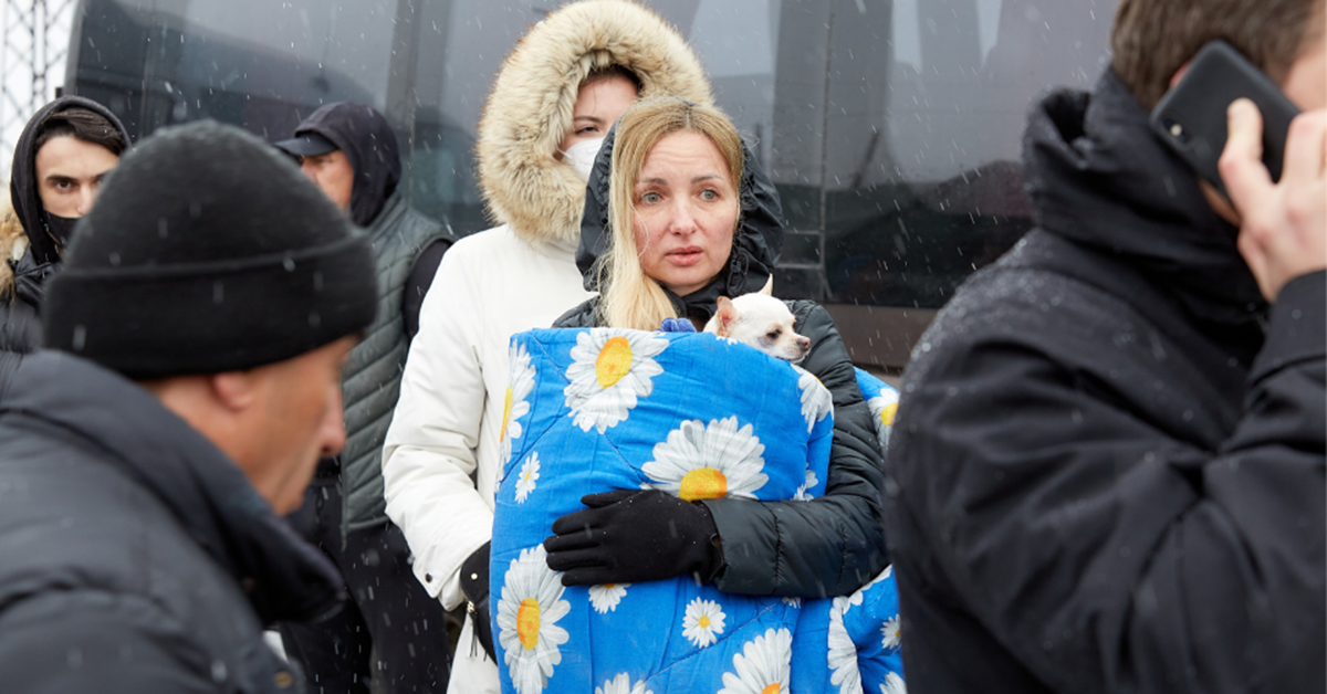 A woman stands in the rain, holding a blanket.