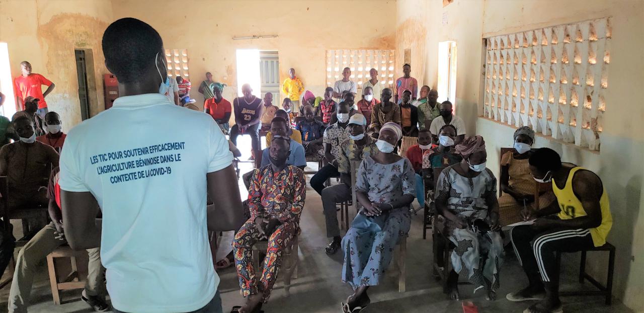 In Benin, a group of men and women attend a training session. They are sitting in a room and listening to a trainer, who is standing before them with his back to the camera.