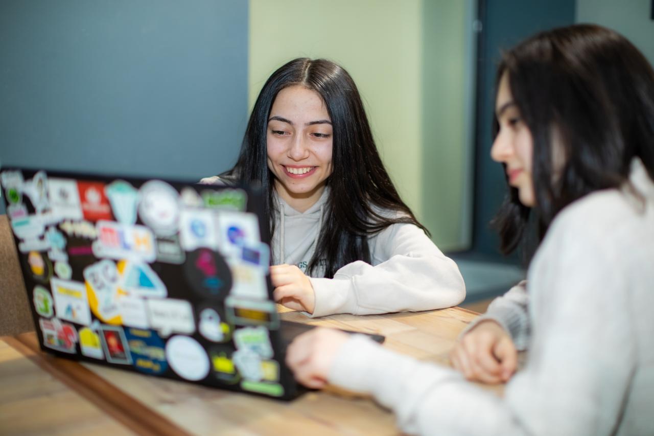 Two girls are sitting at a desk and working on a laptop