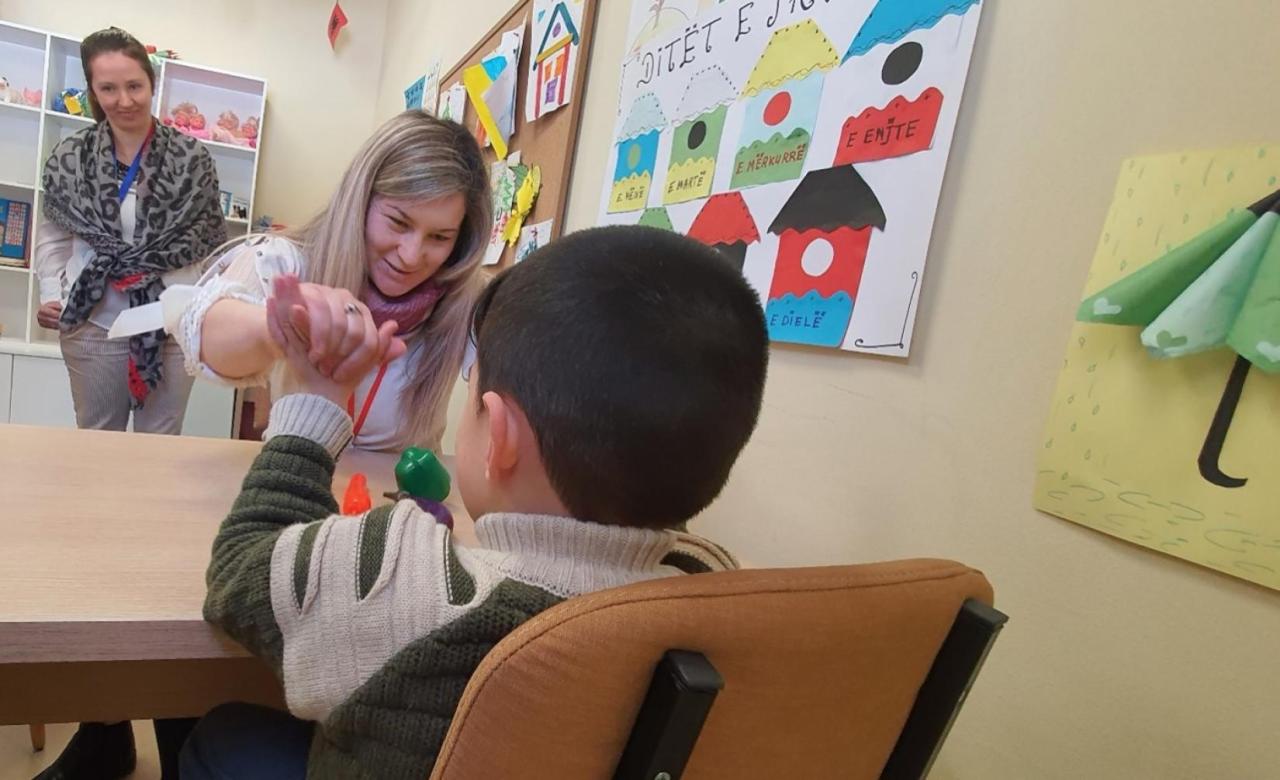 A woman plays with a child over a small table, as another woman looks on.