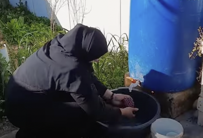 A woman using water from the a plastic tank.