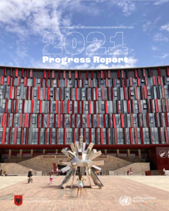 A woman faces a modern art sculpture in front of a red modern-esque building.
