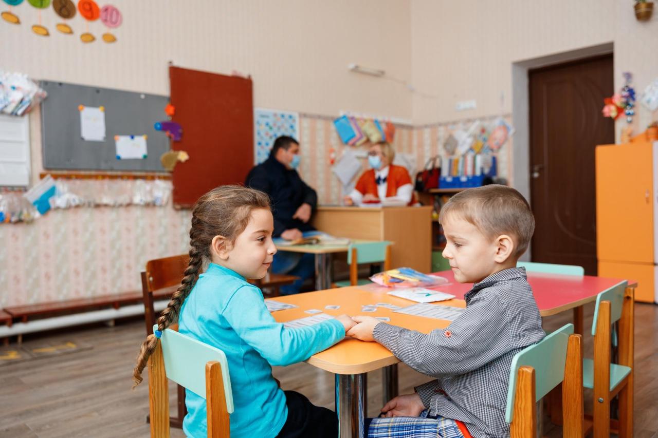 Two little children are sitting at a desk in a classroom. 