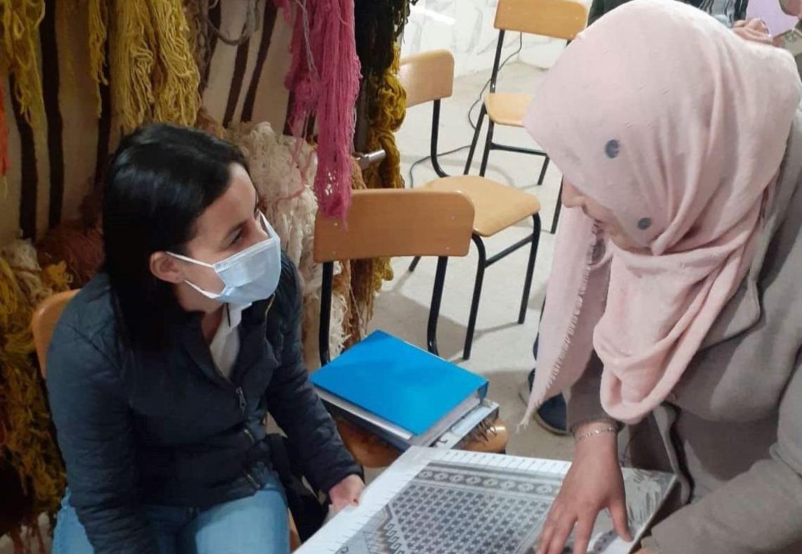 一个穿着牛仔裤、戴着呼吸器的女人与一个戴着面纱的女人讨论她们都拿着的一个模型。