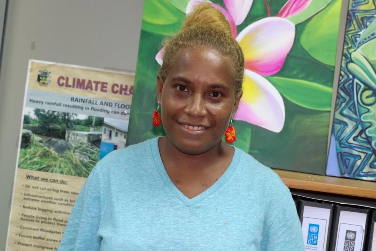 A youth activist in a blue t-shirt and red earrings smiles.