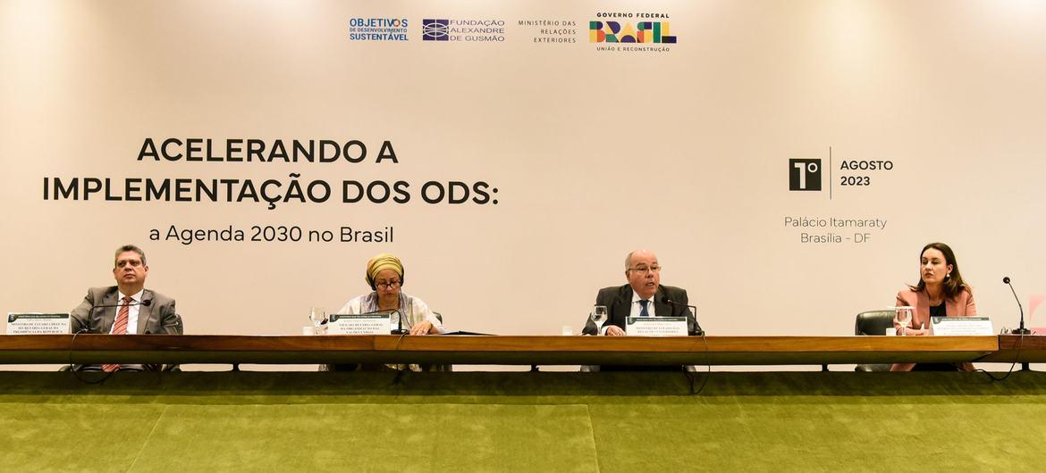 Four people sit on a podium above a green table