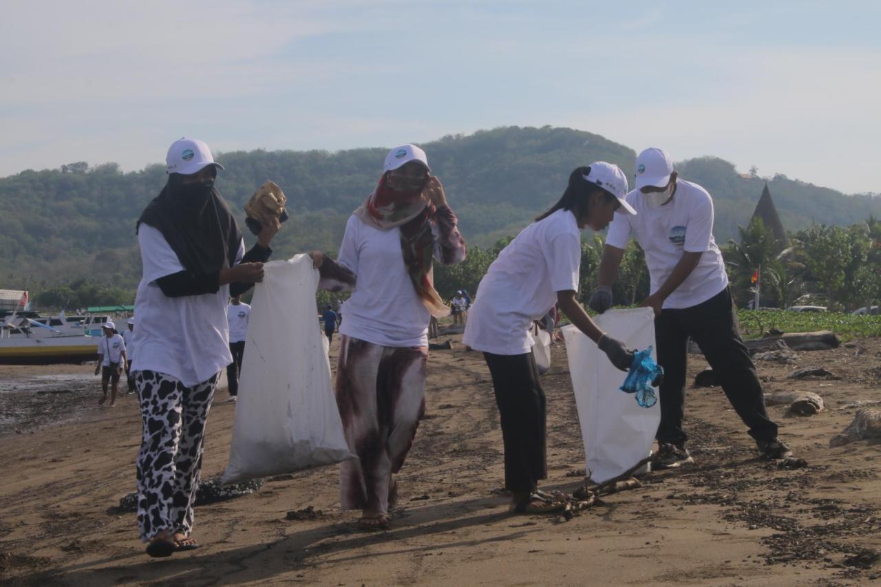 Volunteers wearing white-brimmed hats pick up litter and clean up a beach