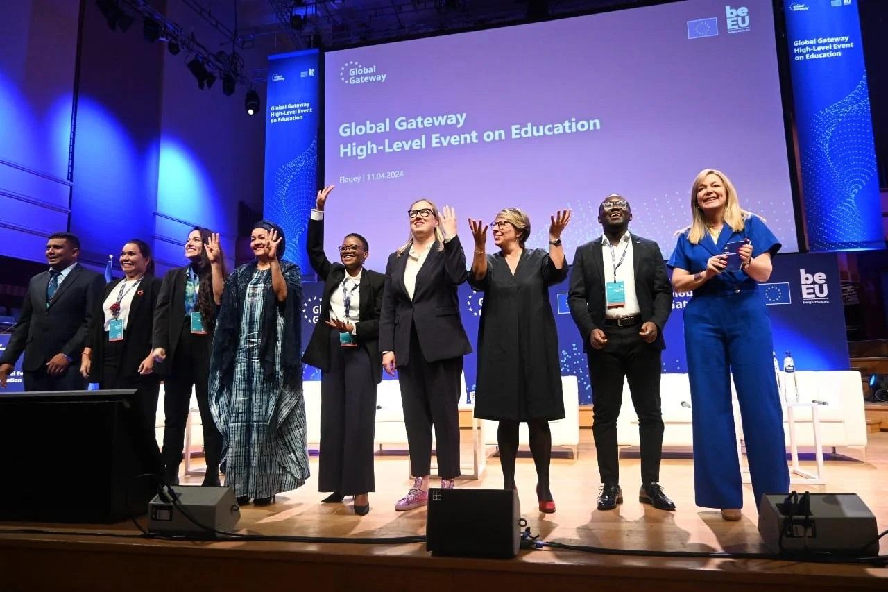 A group of people both men and women stand on stage and wave at an audience in front of them