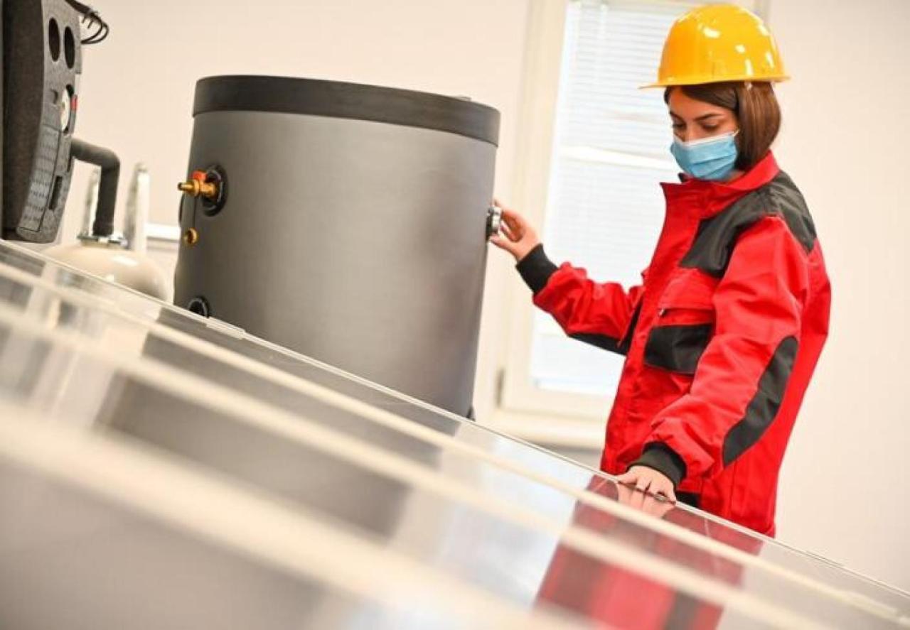 A person in an orange safe suit and yellow hard hat examines a grey solar panel