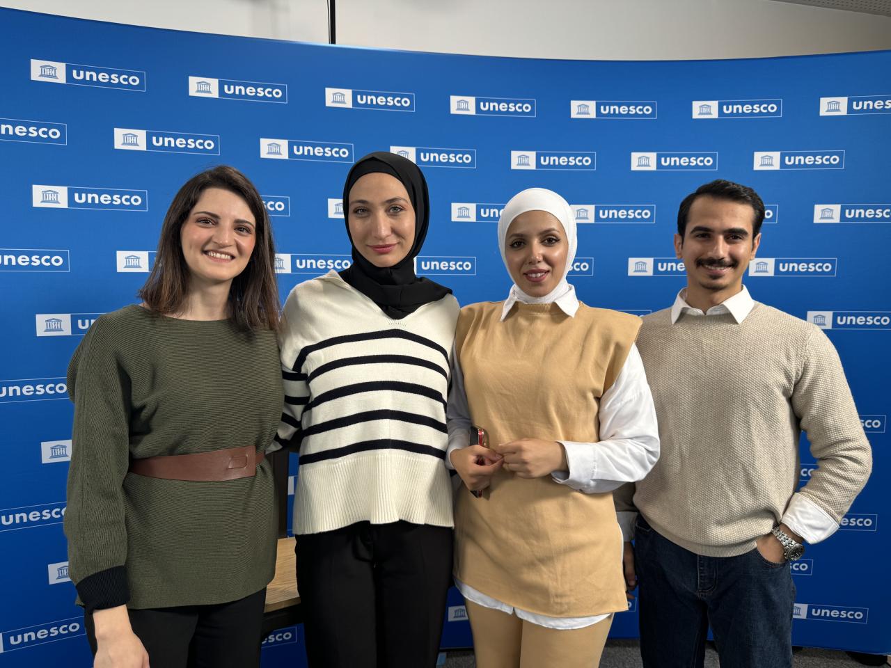 A group of three women and one man stand in front of a backdrop that has the UNESCO logo on it 