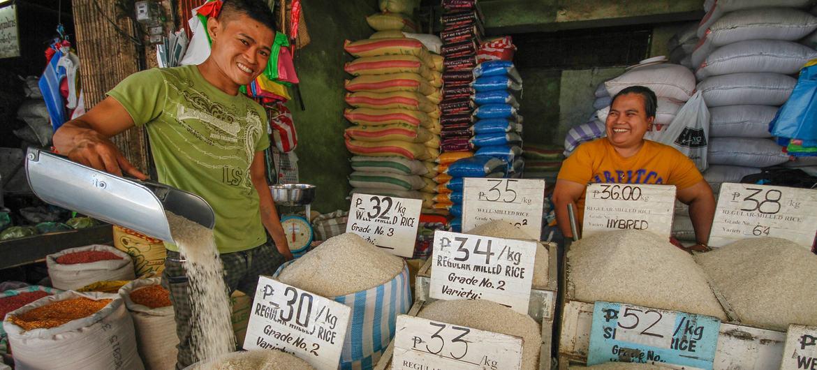 Two people at a food market, one pouring grains into a bucket.