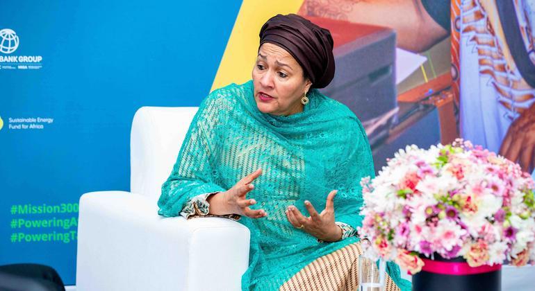 Woman in a green dress and purple headscarf gestures as she speaks in a meeting