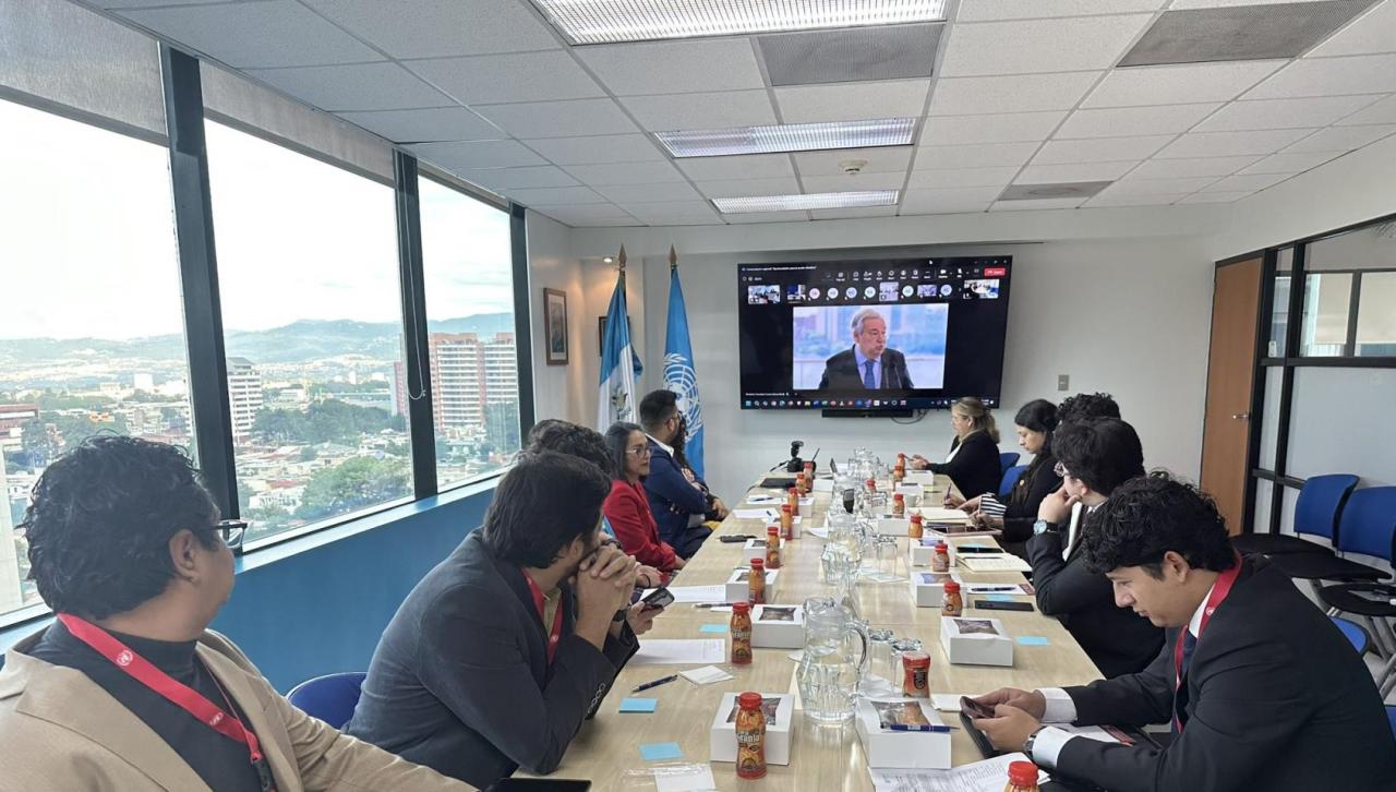 A group of young people around a table watching the Secretary-General on a screen