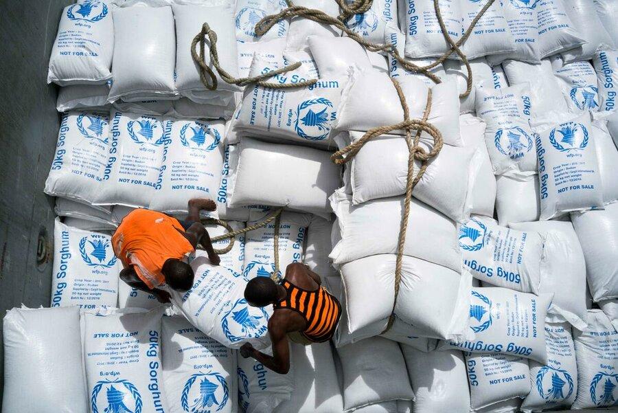 Two humanitarians deliver bags of sorghum.