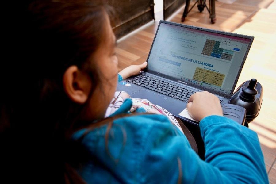 Una mujer, sentada en una silla de ruedas eléctrica, revisa un documento en su computadora.