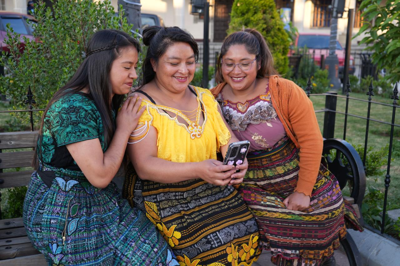 Three women in Guatemala look at something on a cell phone together.