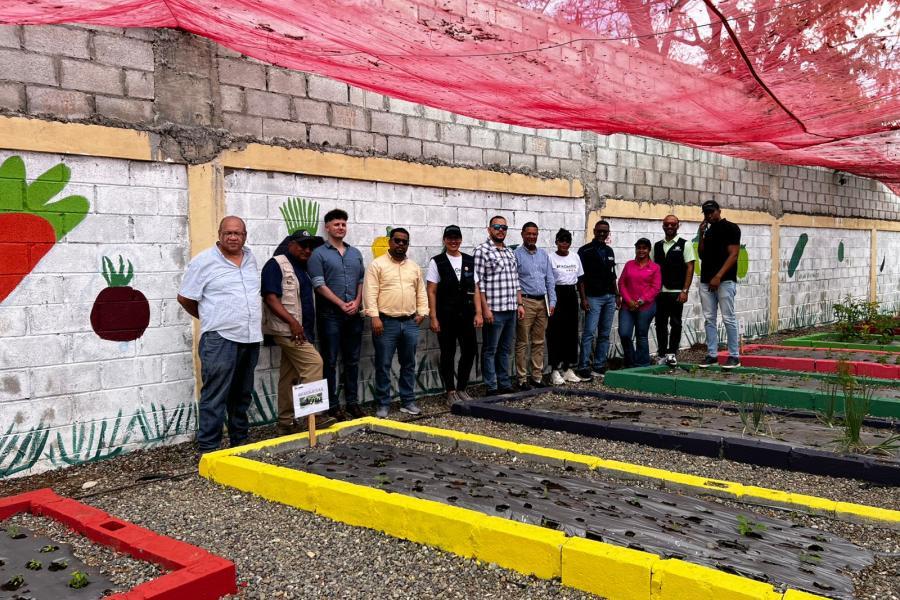 Un grupo de personas posa junto a bancales de cultivo en un huerto comunitario.