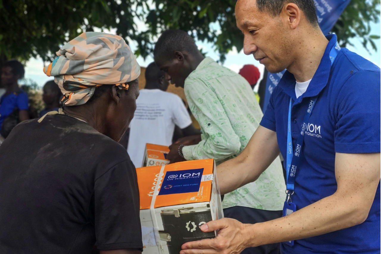 An IOM employee in Malawi distributes a clean cookstove to a resident of a relocation site.
