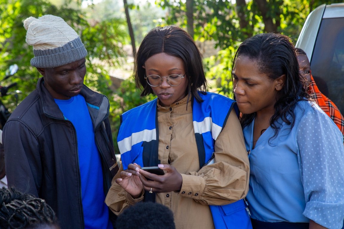 Two women and a man in Kenya look at a phone.