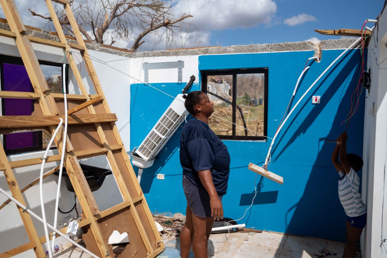 A woman stands in a destroyed house with her son.