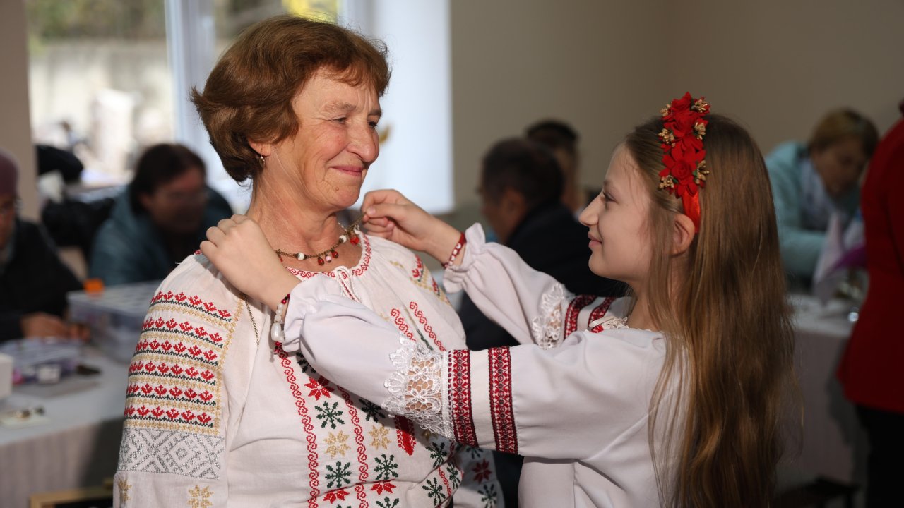 A girl puts a necklace on an elderly woman's neck.
