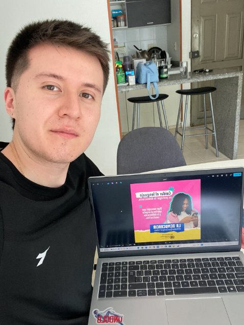 Un joven posa junto a un ordenador portátil que muestra una campaña sobre democracia y ciudadanía digital.