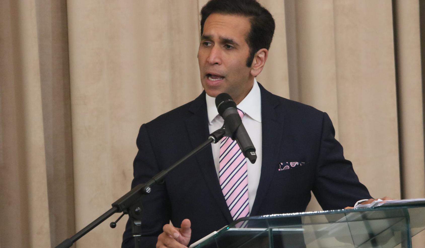 Faris Al-Rawi, Fiscal General de Trinidad y Tobago, se muestra hablando por un micrófono en un podio en el escenario.