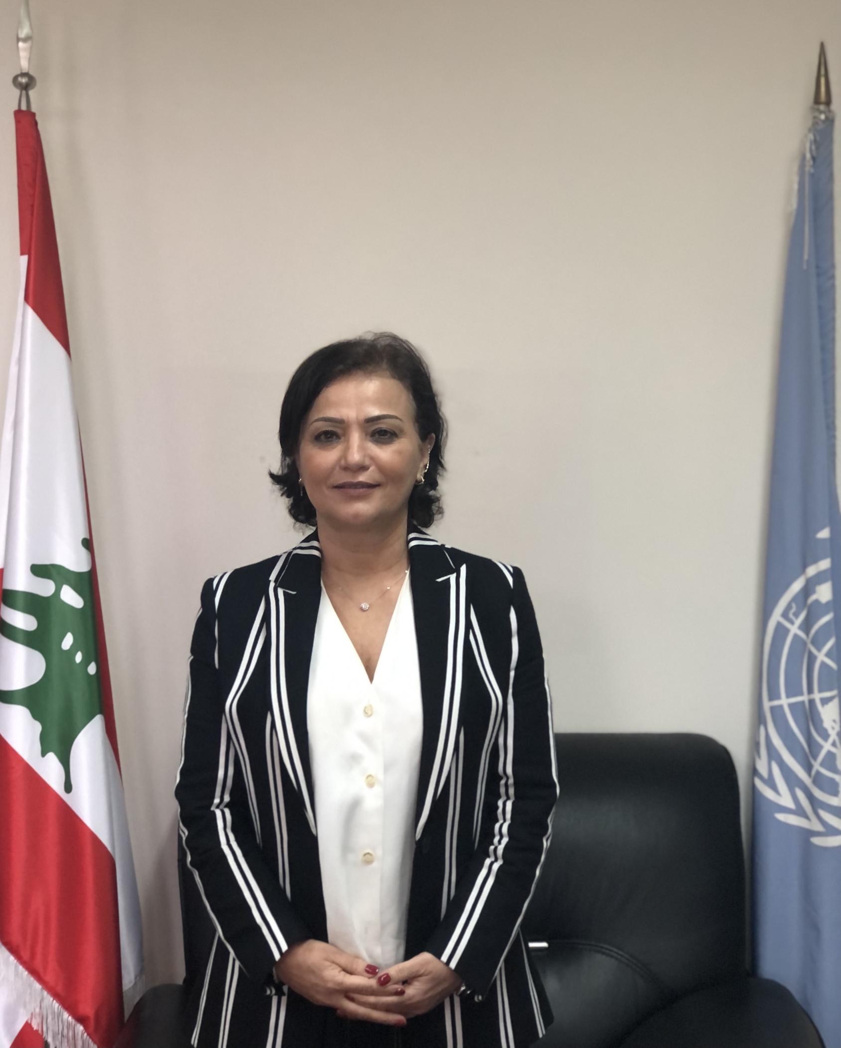 An image of Najat Rochdi standing in between two flags. 