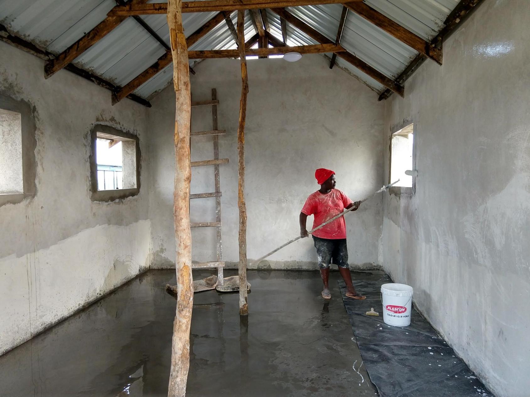 A person in a red shirt and hat paint the walls of a building. 