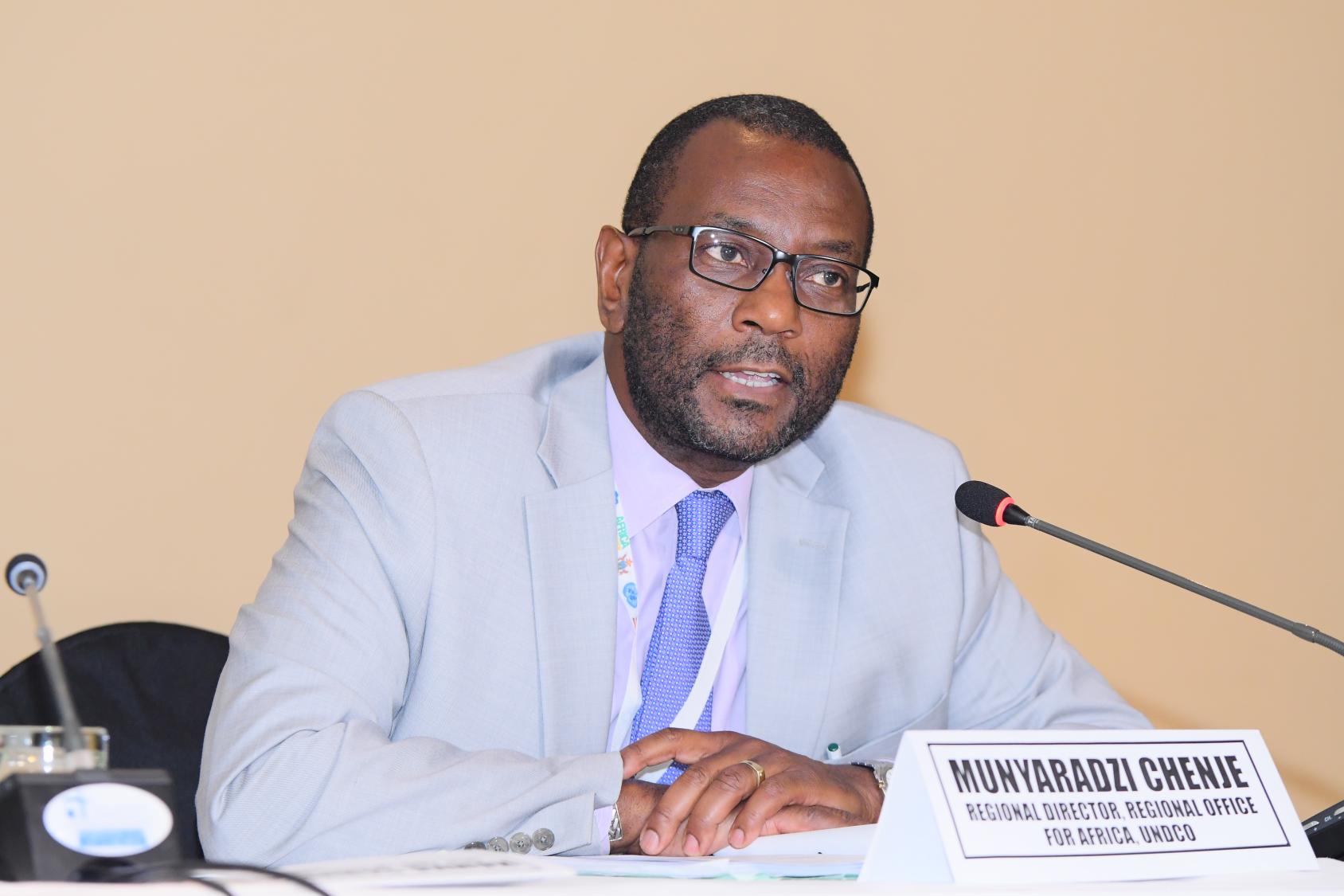 Mr. Chenje speaks into a microphone at a conference. 