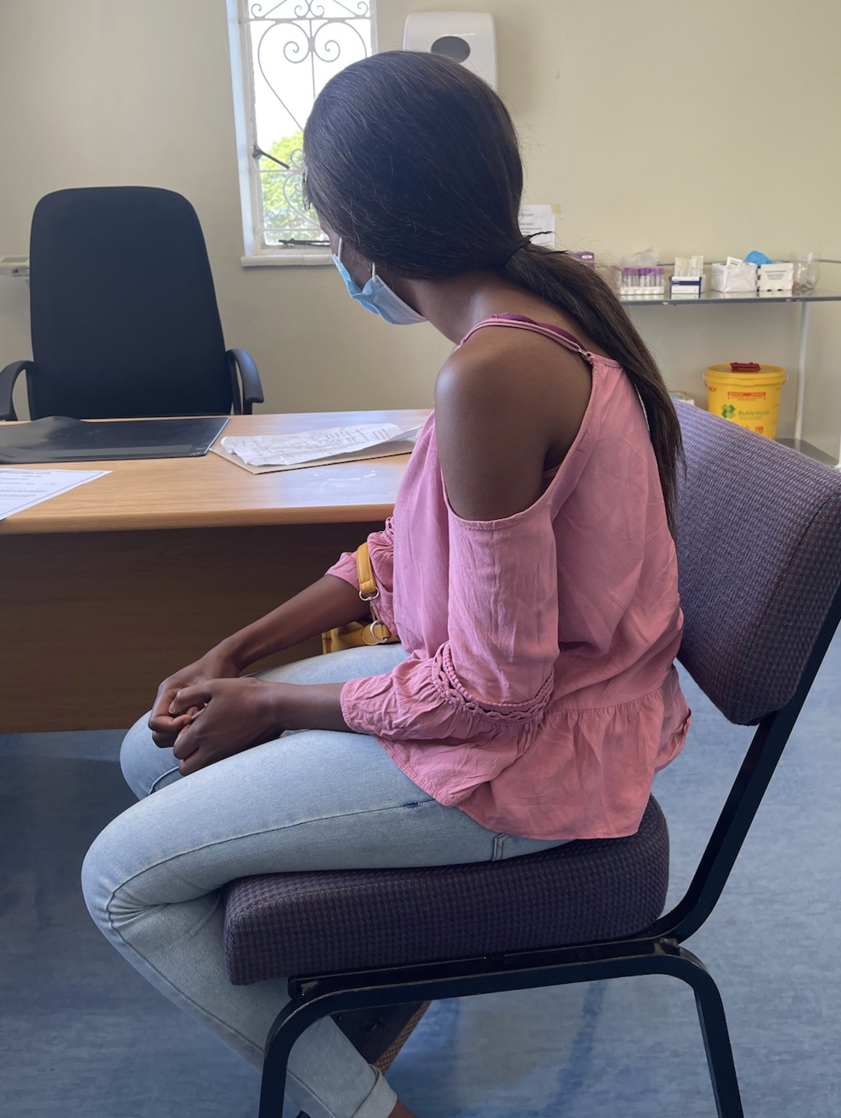 在一家诊所里，一名身穿粉红色衬衫和牛仔裤的妇女背向镜头。