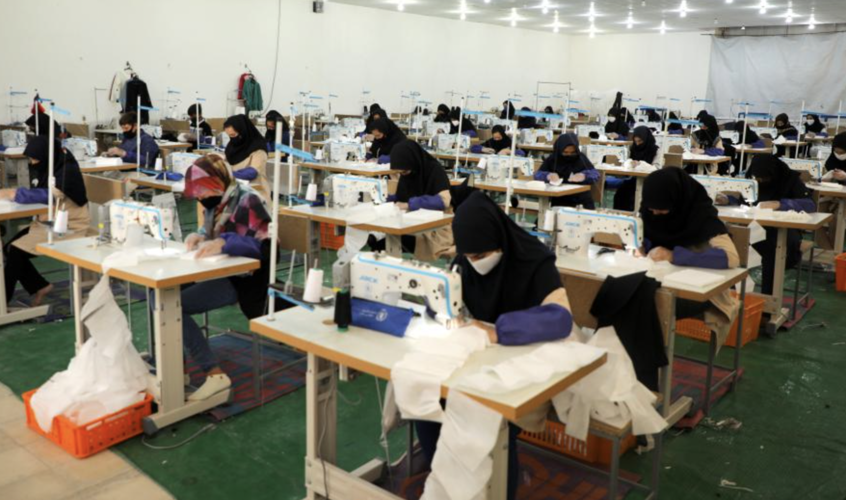 Un gran cantidad de profesionales de la confección trabajan en pequeñas mesas, con su correspondiente máquina de coser.