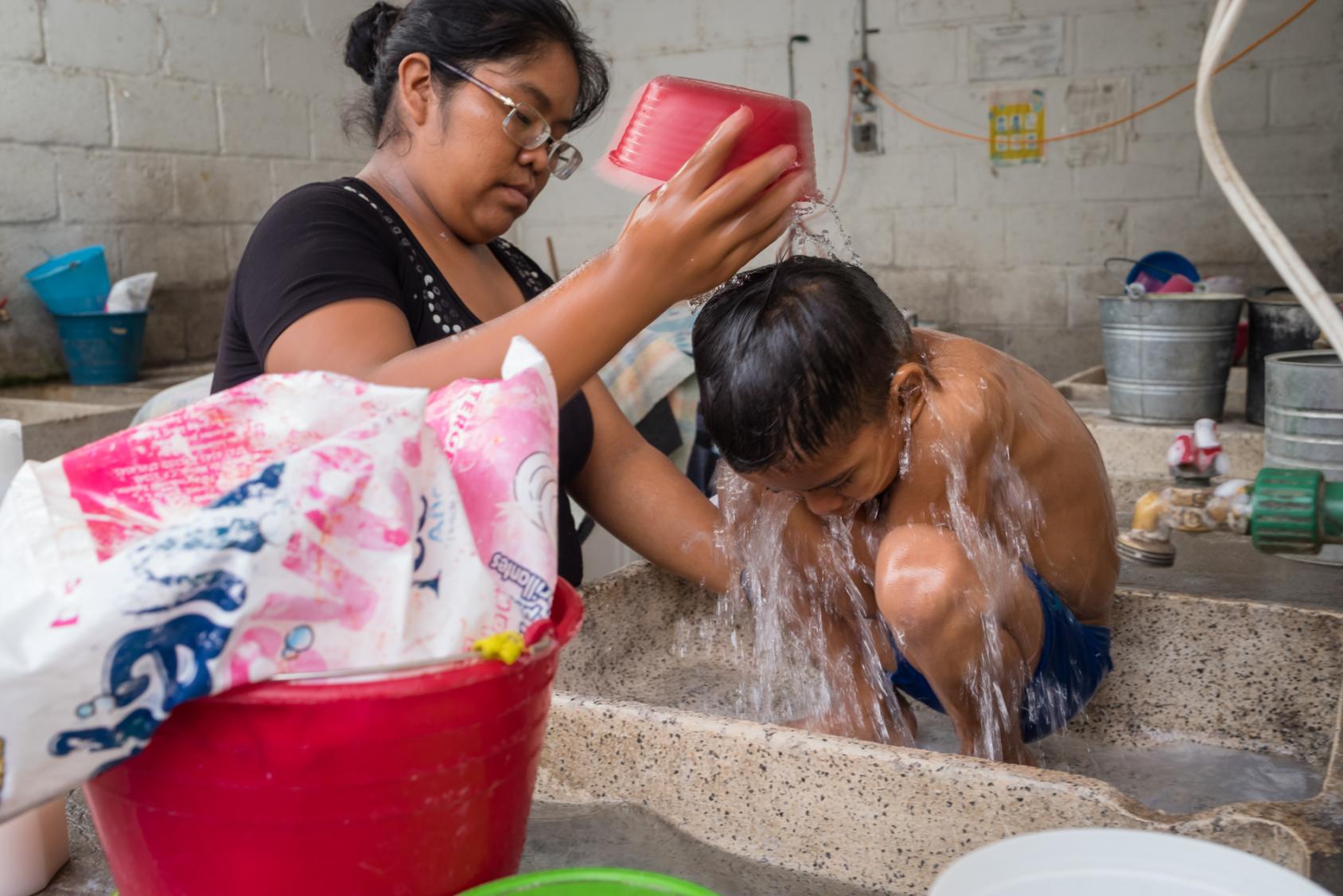 A woman in a black shirt bathes her son in a sink. 