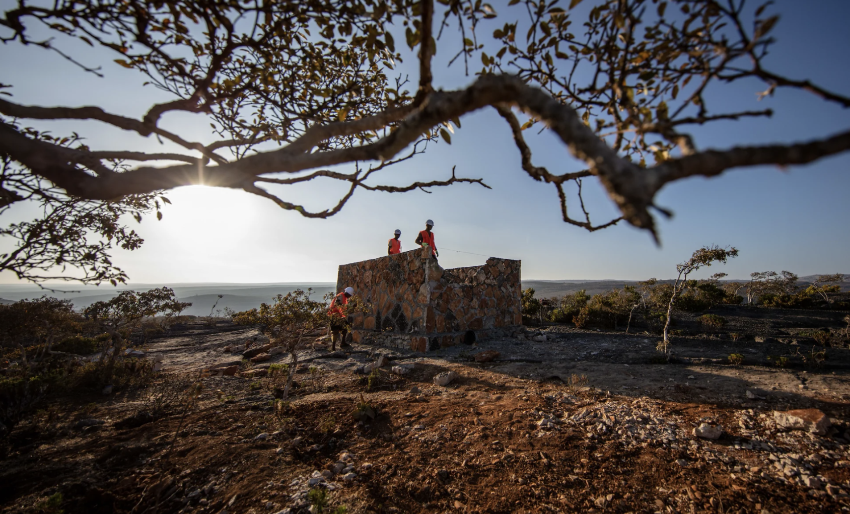 Tres trabajadores de la construcción de pie sobre una estructura cuadrada de ladrillos.