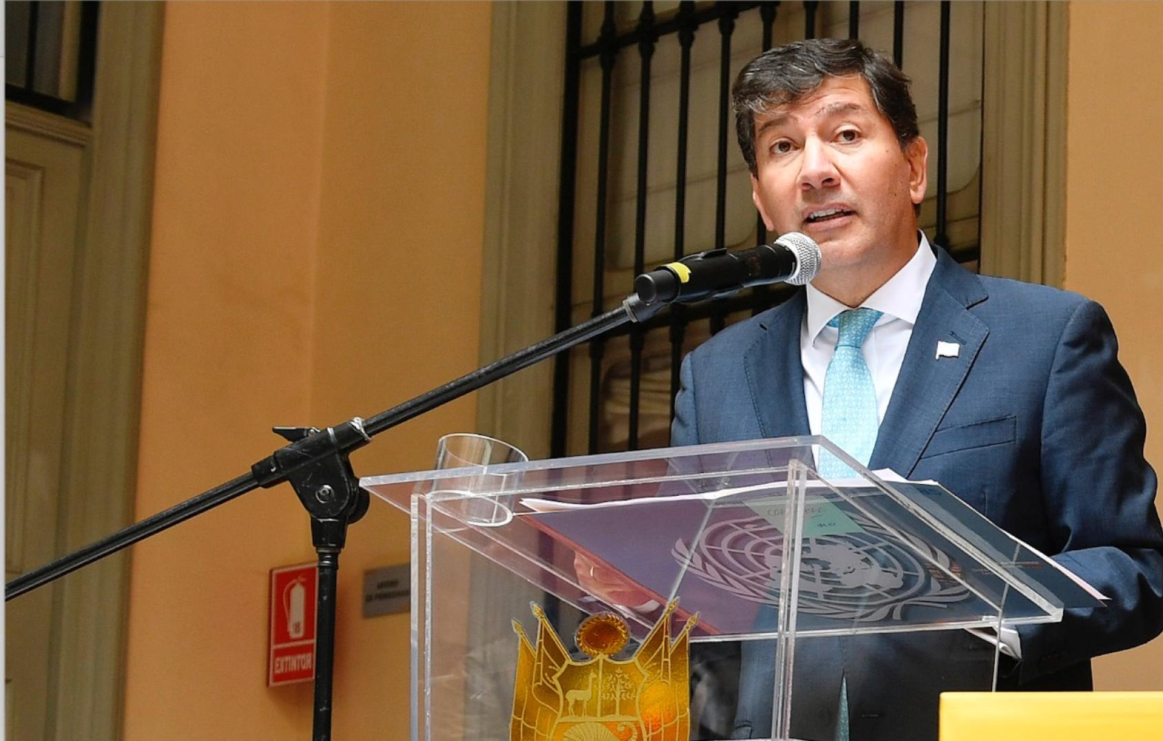 رجل يتحدث أمام الميكروفون مرتديًا بدلة زرقاء وربطة عنق.