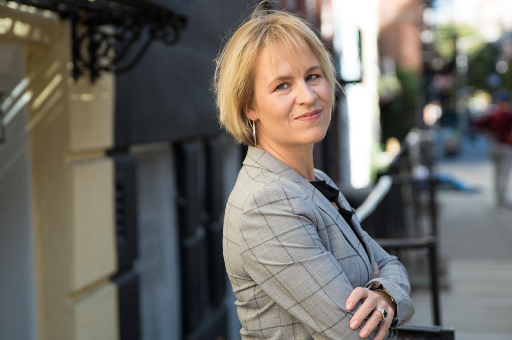 صورة لامرأة تقف في الهواء الطلق وتنظر إلى الكاميرا مكتوفة اليدين.