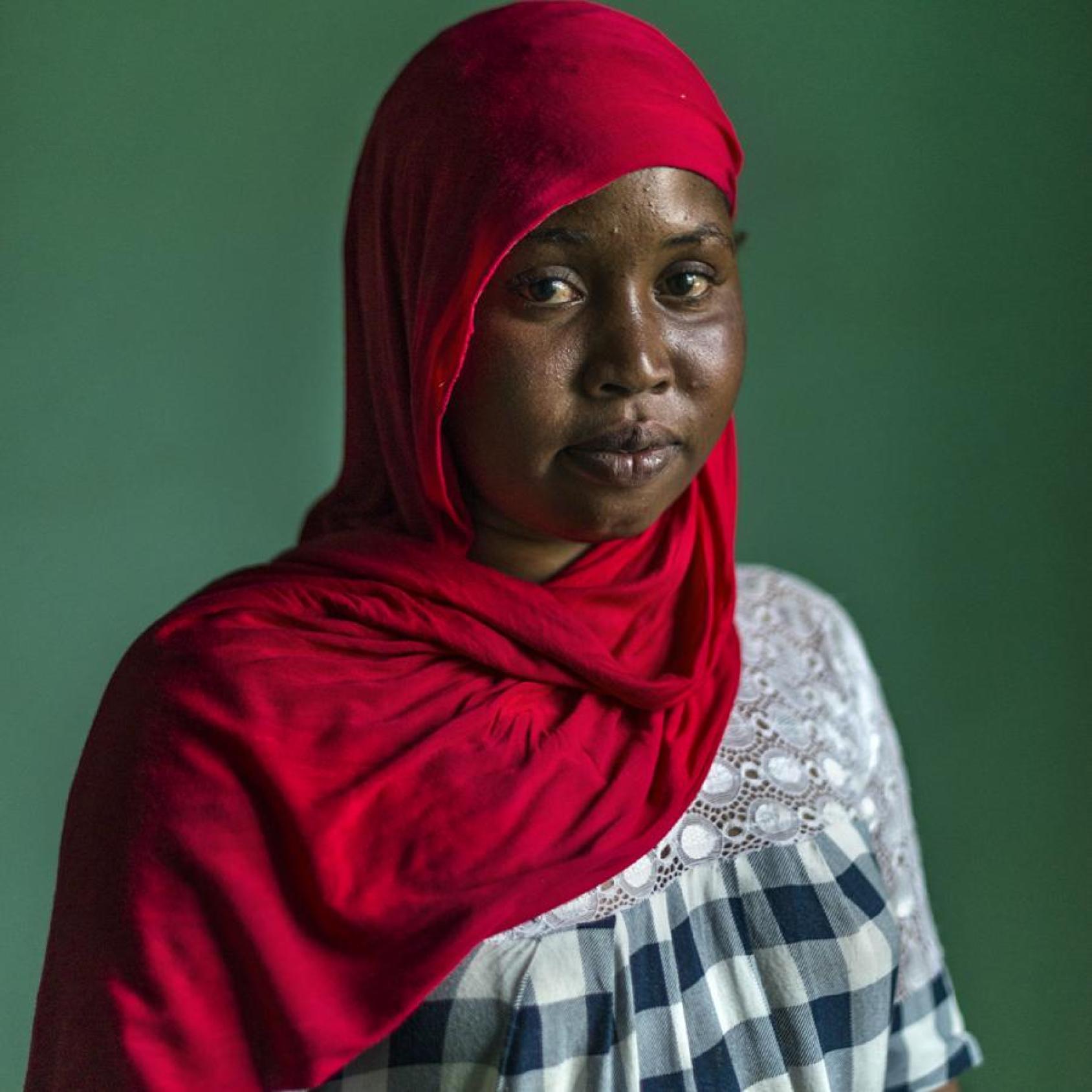 Una mujer con un pañuelo rojo, que le cubre la cabeza, mira directamente a la cámara.