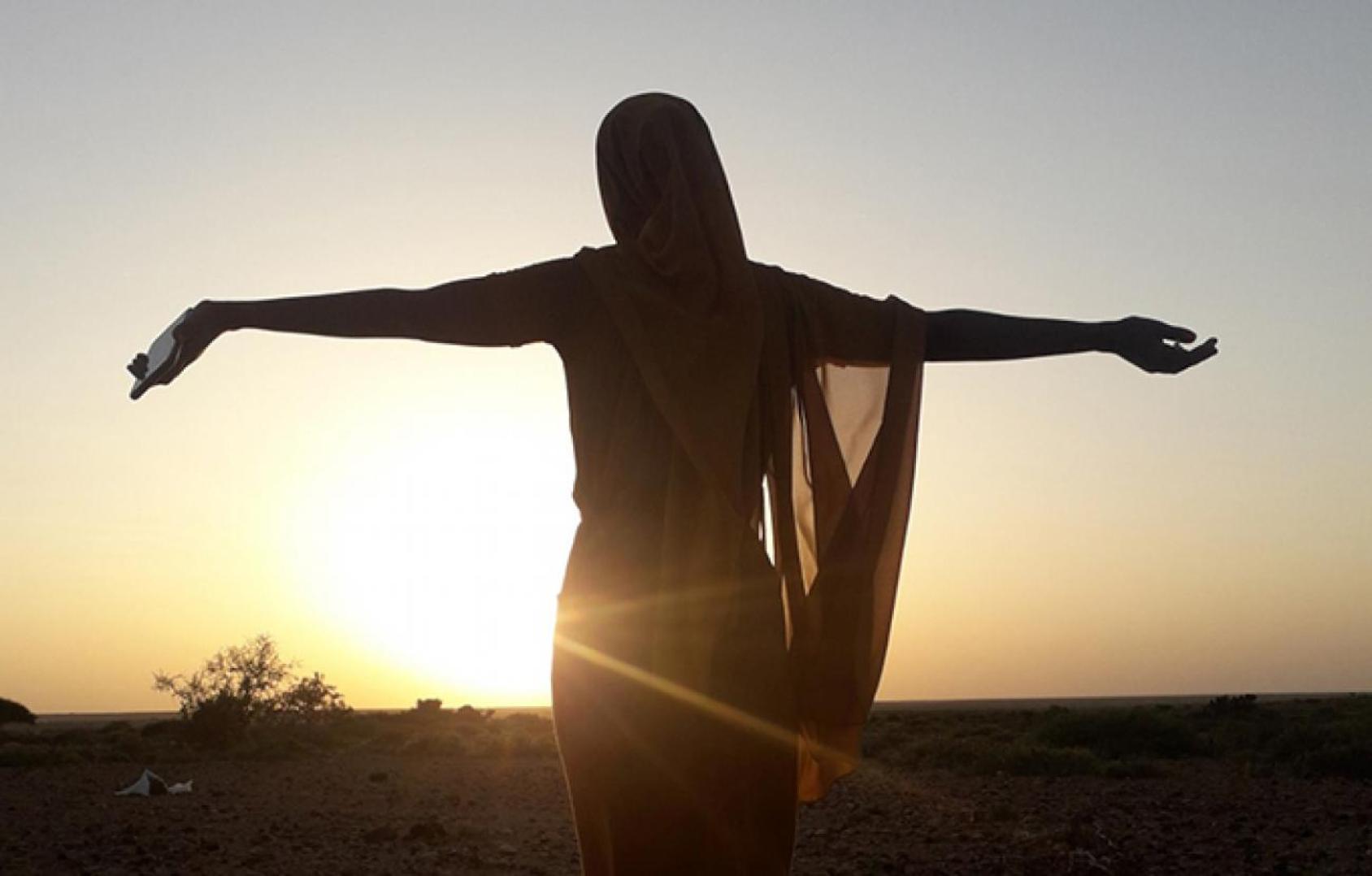 صورة ظلية لامرأة تنظر إلى غروب الشمس.