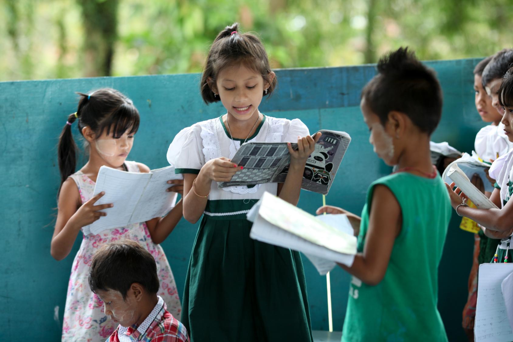 Des enfants, debout sur la terrasse d'un établissement scolaire, lisent des manuels.