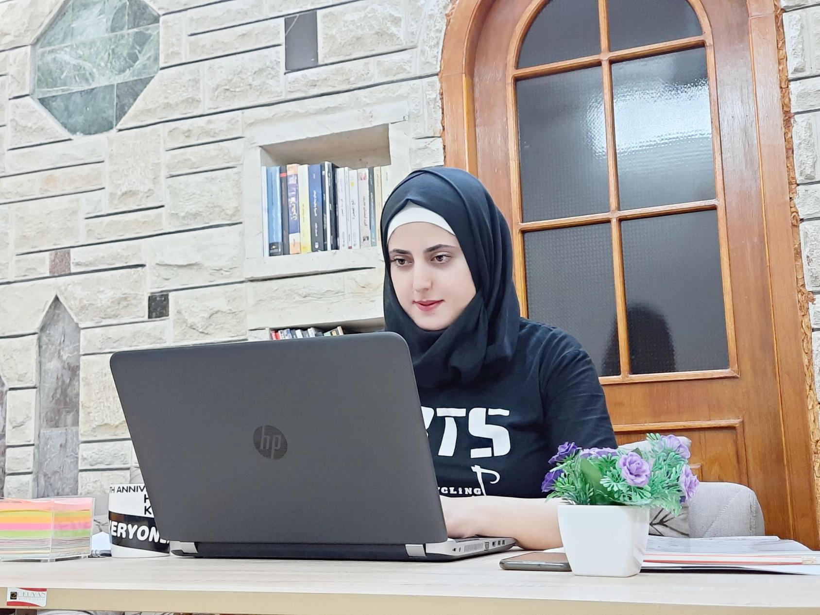 شابة تجلس أمام حاسوب محمول قرب النافذة.