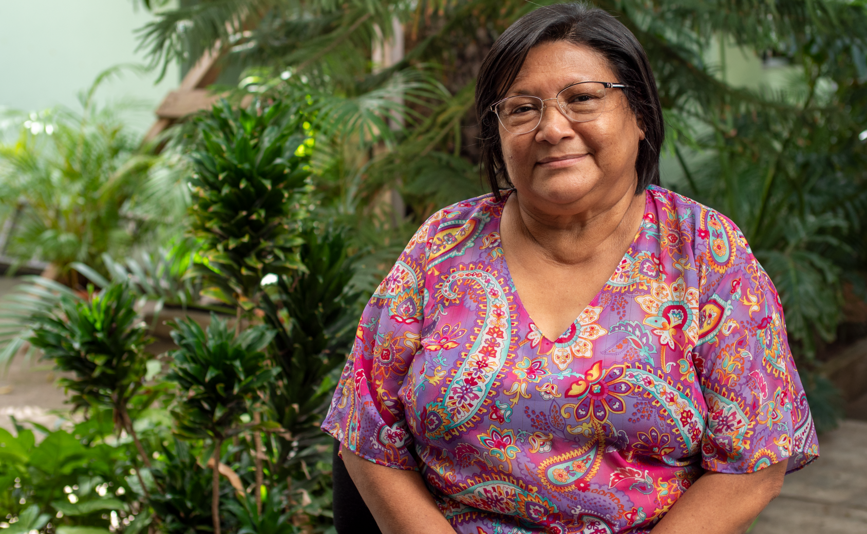 تبتسم امرأة للكاميرا وهي جالسة أمام أشجار صغيرة.