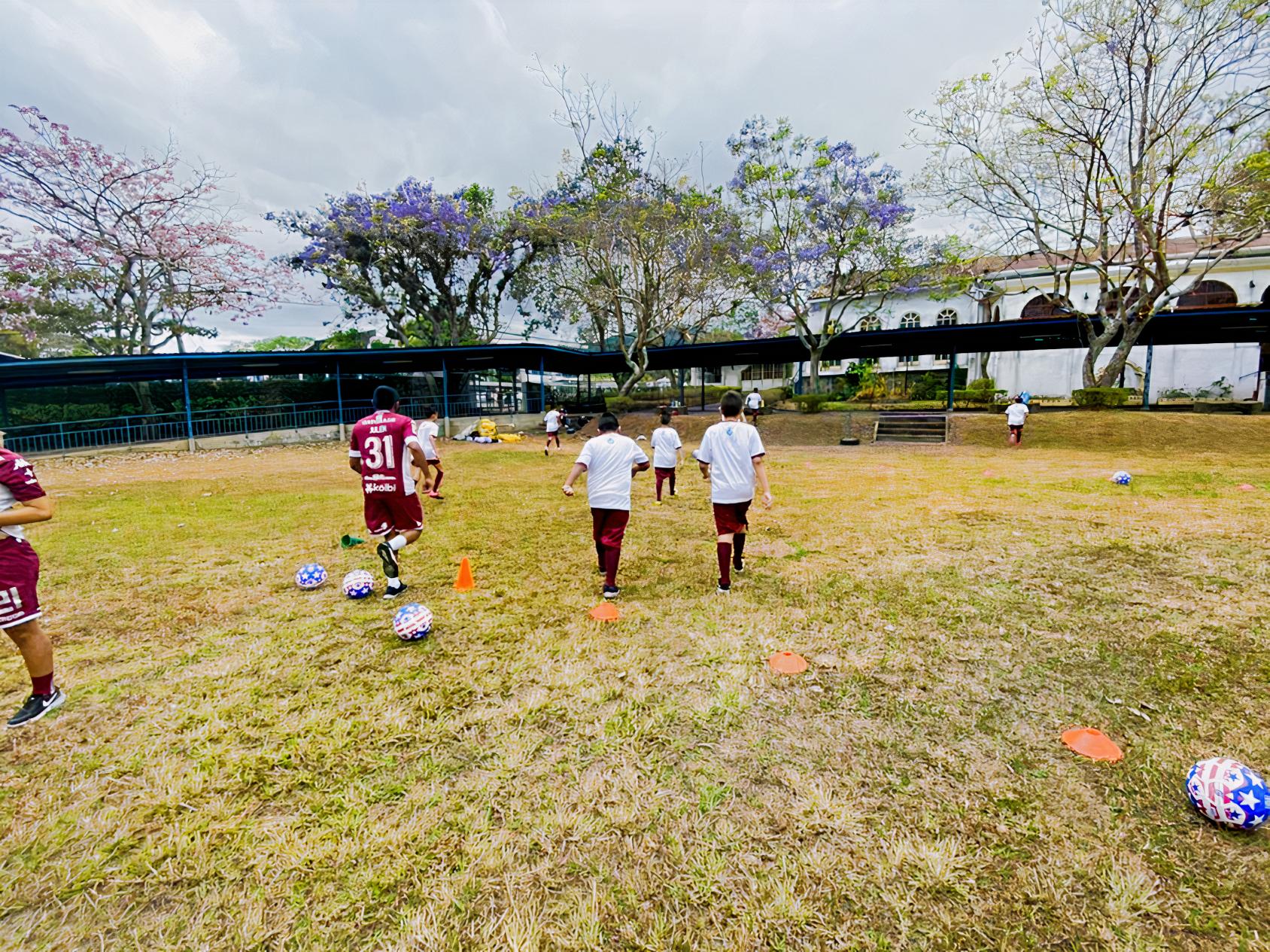 Au Costa Rica, des enfants jouent au football sur un terrain de jeu entouré d’arbres par temps nuageux.