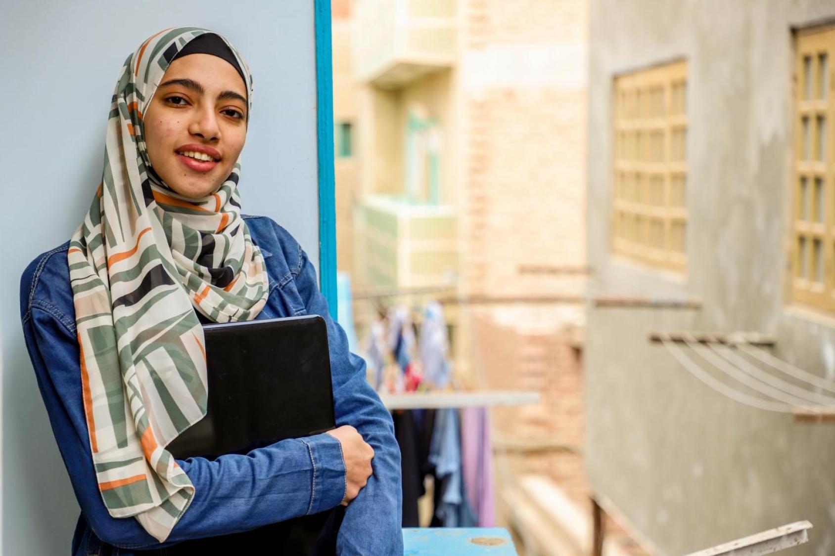 A girl looks straight at the camera while holding a laptop in her arms. 
